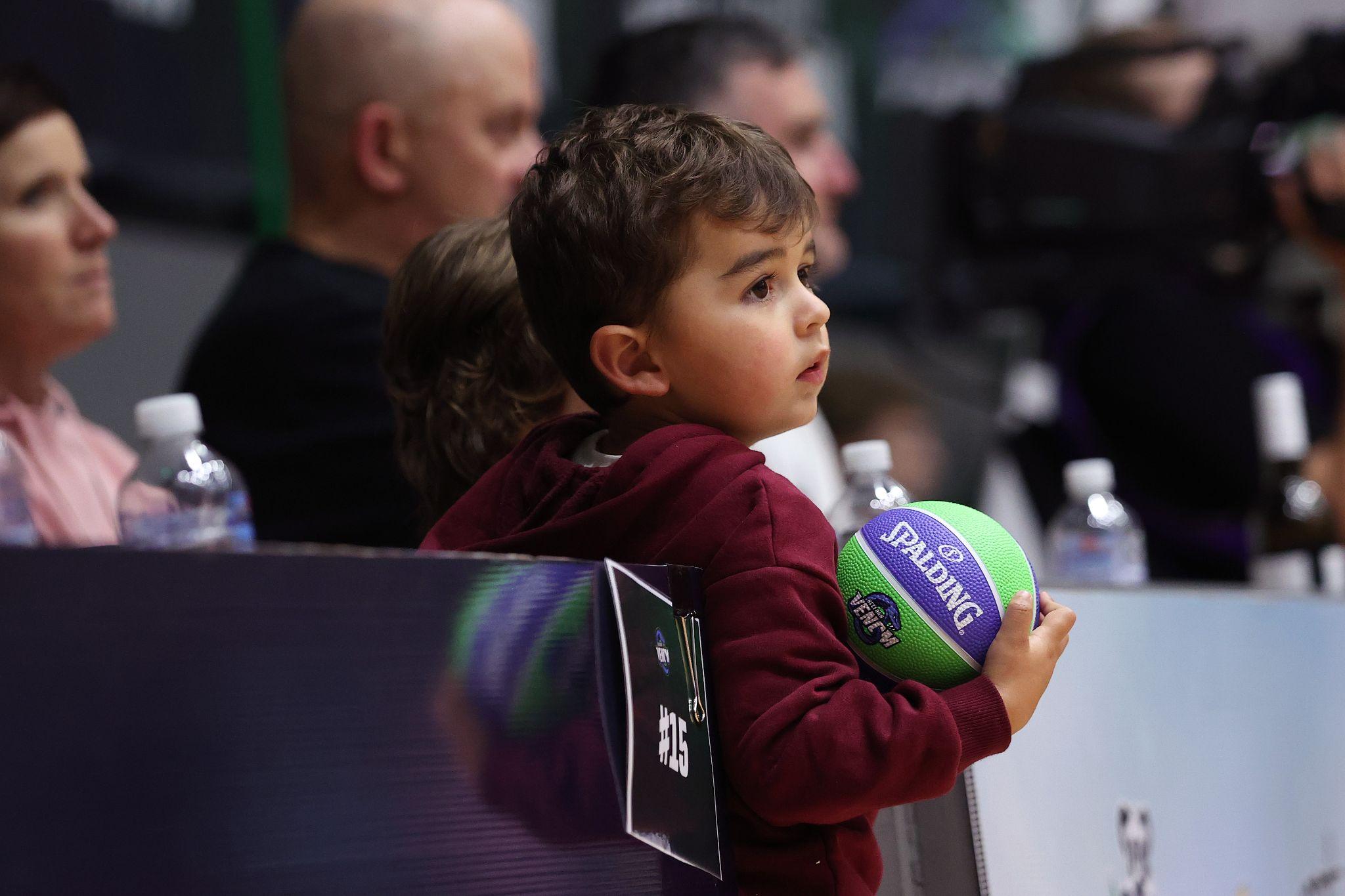 A young supporter holding a basketball while watching a Geelong Venom game courtside